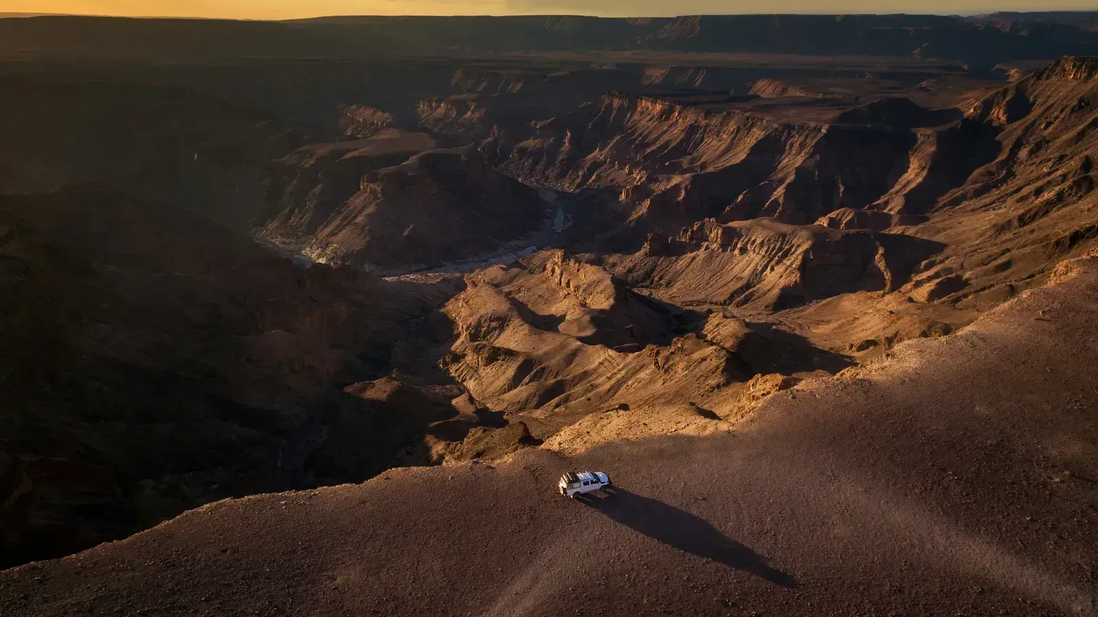 A lone 4x4 pauses on the rim as sunset floods the canyon